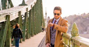 An elegant man standing on a bridge and checking the time.